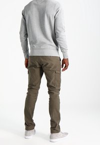 Grauer Pullover mit V-Ausschnitt und gerippten Bündchen, kombiniert mit olivgrünen Cargo-Hosen mit Seitentaschen und hellgrauen Turnschuhen.