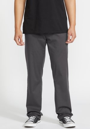 Graue Hose aus leichtem Stoff, mit geradem Bein, Seitentaschen und getragen mit schwarzen Sneakers.