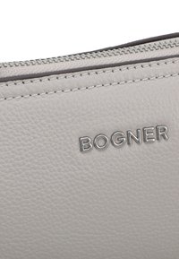 Siva usnjena torbica z teksturirano površino, ki ima srebrno obarvano logo "BOGNER" in kontrastno zadrgo ob zgornjem robu.