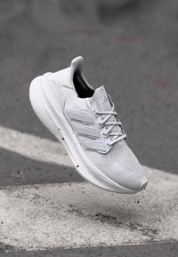Weißer Sportschuh mit Obermaterial aus Mesh und Synthetik, ausgestattet mit drei Streifen, Schnürverschluss und gepolsteter Sohle. Leicht mit strukturierten Akzenten.