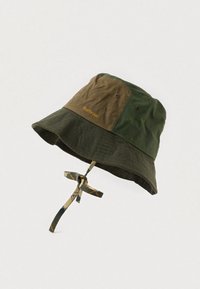 Πράσινο και καφέ πλεκτό καπέλο μπucket με ραμμένη χείλη, αεραγωγούς και μια καρό λουρί για το πηγούνι δεμένο σε φιόγκο.