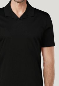 Czarna koszulka polo z krótkim rękawem, klasycznym kołnierzykiem i gładkim, lekkim materiałem. Posiada subtelny detal w postaci szwu przy dekolcie.