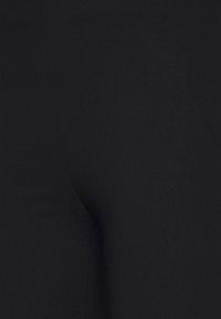 Gros plan sur un tissu noir avec des coutures visibles, montrant une texture lisse et une légère élasticité.