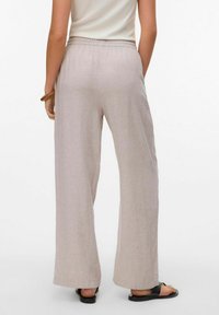 Lichtbeige, culotte-pantalons van zachte stof, met een elastische tailleband en een gladde textuur, gedragen met zwarte sandalen.