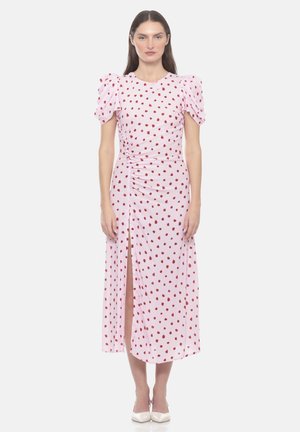 Donna che indossa un vestito midi rosa con pois rossi, maniche corte a sbuffo, uno spacco frontale e tacchi bianchi a punta, in piedi su sfondo bianco.