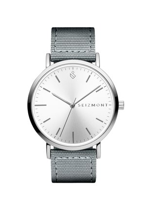 Minimalistisk armbåndsur med sølvfarget urskive, tynne timemarkører, tre visere, grått stoffarmbånd og "SEIZMONT"-logo på urskiven.