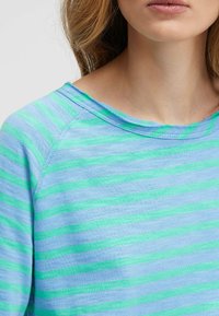 Leichtes, gestreiftes Hemd in Blau- und Grüntönen. Verfügt über einen weiten Ausschnitt und Raglanärmel aus einem strukturierten Stoff mit unregelmäßigem Saum.