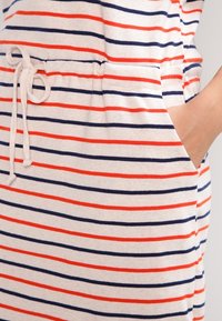 Vêtement rayé en tissu léger avec des lignes horizontales bleu marine et rouges. Doté d'une taille à cordon de serrage et de poches lat érales.