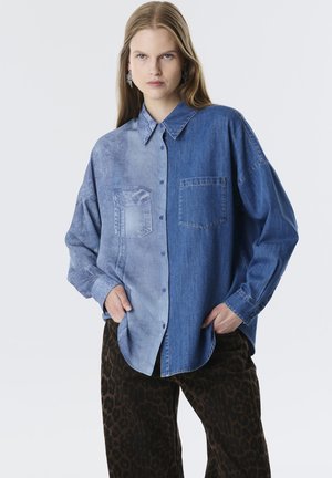 Jeanshemd mit einem zweifarbigen Design: eine Seite hellblau mit einer Textur, die andere Seite dunkelblau. Lange Ärmel, Knopfverschluss.