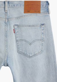 Jeans de mezclilla azul claro con un parche de cuero en la cinturilla, que presentan un único bolsillo trasero y detalles de costura en hilo en contraste.