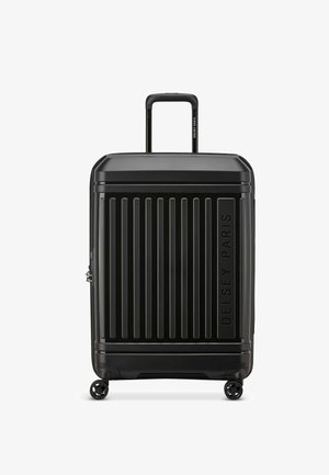 Valise rigide noire avec des rainures verticales, poignée extensible et quatre roues. Présente le logo embossé "Delsey Paris" à l'avant.