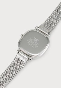 Montre carrée en acier inoxydable avec un bracelet en maille métallique. Dos gravé avec des détails, y compris le numéro de modèle et les informations de résistance à l'eau.