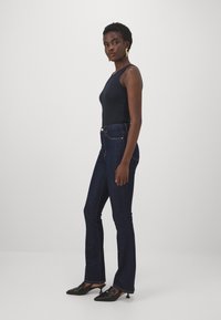 Top sin mangas azul marino combinado con jeans de campana de lavado oscuro y mule de tacón negro. El conjunto presenta una silueta ajustada y líneas limpias.