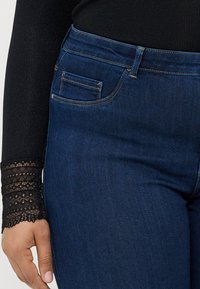 Jeans de denim azul-escuro com um design padrão de cinco bolsos, cintura média e detalhes de costura subtis.
