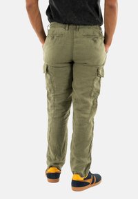 Pantaloni cargo verde oliva con vita elasticizzata, molteplici tasche laterali e una vestibilità leggermente libera, abbinati a scarpe navy con dettagli arancioni.