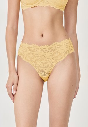 Tanga en dentelle jaune avec motif floral, bords festonnés et texture semi-transparente. Le tissu doux offre une apparence délicate et légère.