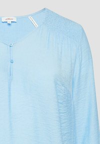 Lichtblauwe blouse met een v-hals, twee knopen en een gerimpelde schouderpartij. Gemaakt van een gewoven stof met een relaxte pasvorm en lange mouwen.