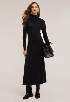 Schwarzes langärmliges Kleid mit hohem Kragen, geripptem Muster, körperbetonter Passform und ausgestelltem Rock. Kombiniert mit einer schwarzen Handtasche und kniehohen Stiefeln.