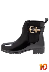 Botín negro de goma hasta el tobillo con un acabado brillante, con un acento de hebilla dorada y panel lateral elástico para mayor flexibilidad. Suela plana con textura antideslizante.