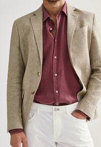Beżowa lniana marynarka z klapami, połączona z bordową koszulą zapinaną na guziki i białymi spodniami, cechująca się subtelną teksturą i eleganckim designem.