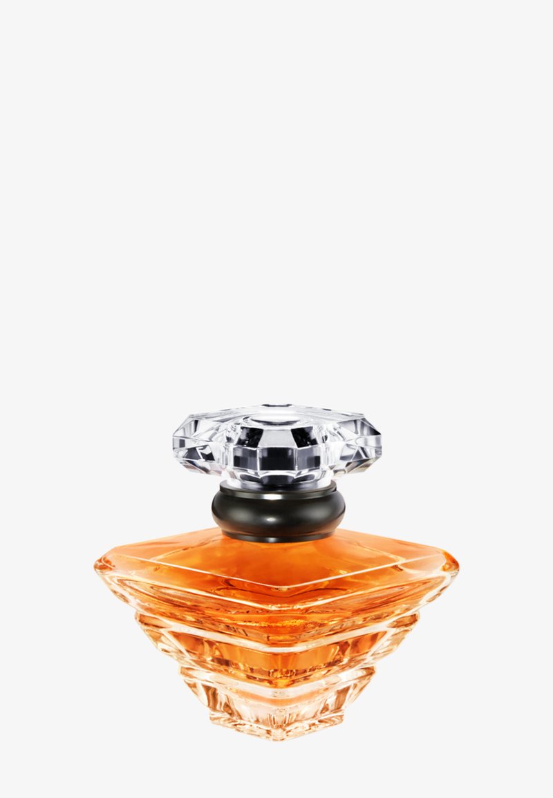 Flacon de parfum en verre transparent avec un liquide orange à l'intérieur et un bouchon transparent facetté sur le dessus.