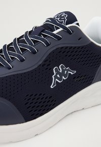 Temno modri mrežasti športni copat z belimi poudarki, z teksturiranimi stranicami, okroglo konico in logotipom v kontrastni barvi na zunanji strani.