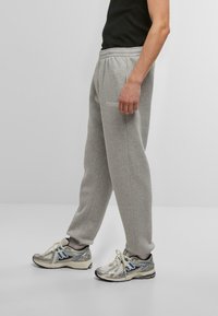 Gray sweatpants made of cotton blend, featuring an elastic waistband and side pockets. A small logo is embroidered on the left thigh.