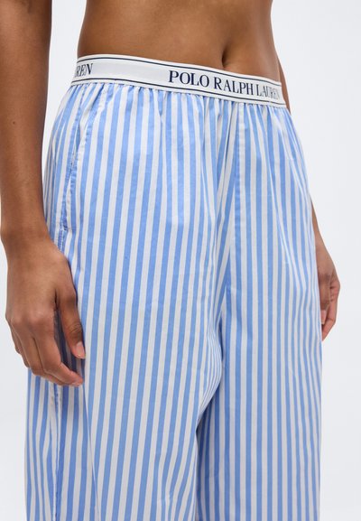 Κοντινό πλάνο ενός ατόμου που φοράει παντελόνια με κάθετες ρίγες σε ανοιχτό μπλε και άσπρο, με λευκή ζώνη μέσης που φέρει την ετικέτα «Polo Ralph Lauren».