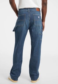 Denim cargobroek in medium blauw met een relaxte pasvorm, voorzien van meerdere zakken, contrasterende stiksels en een leren label bij de taille.