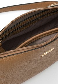Intérieur d'un sac à main en cuir texturé marron avec plusieurs compartiments et une fermeture éclair. Présente des éléments en doré et un accent avec un logo.