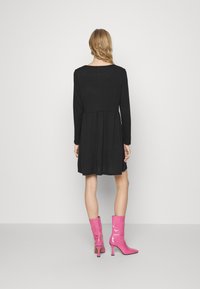 Schwarzes langärmeliges Kleid mit tailliertem Oberteil und ausgestellt Rock, kombiniert mit glänzenden rosa Knöchelschuhen mit spitzem Zehen und Stiletto-Absatz.