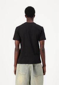 Camiseta de algodón negra con cuello redondo, mangas cortas y un corte relajado, combinada con pantalones de mezclilla holgados de color claro.