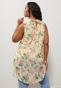 Blusa senza maniche floreale in beige chiaro con motivo floreale pastello, apertura a chiave sul retro con fiocco e orlo arrotondato.