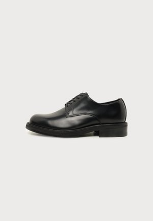 Chaussure de ville pour homme en cuir noir poli avec laçage fermé, bout rond et petit talon sur un fond clair uni.