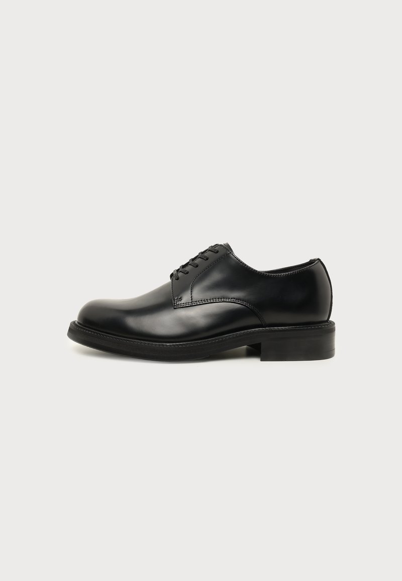 Chaussure de ville pour homme en cuir noir poli avec laçage fermé, bout rond et petit talon sur un fond clair uni.