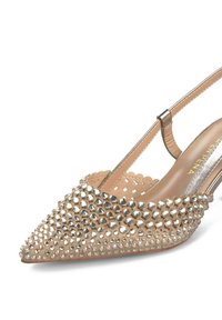 Beige patent leather slingback shoe with pointed toe, adorned with silver studs, featuring a thin ankle strap and cut-out design on the sides.