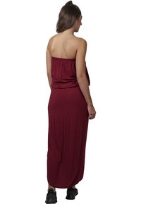 Burgundi off-shoulder maxiruha, laza fazonnal, puha textúrával és rugalmas derékkal. Fekete sportcipővel viselve, egyszerű dizájnnal.