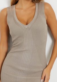 Débardeur beige côtelé avec un col en V et des accents texturés, doté d'une conception sans manches et d'une silhouette ajustée.