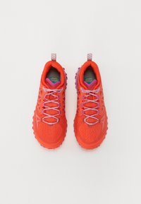 Sapatilhas desportivas vermelhas com parte superior em malha, detalhes em rosa e sola de borracha texturizada. Apresenta atacadores planos e laços na parte de trás para fácil colocação.