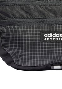 Černý batoh Adidas Adventure s texturovanou tkaninou a mřížkovým vzorem, s kapsami na zip a výraznou logovkou.