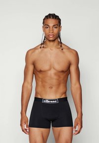 Schwarze Boxershorts aus glattem Stoff mit breitem elastischem Bund, der ein weißes Logo trägt. Das Design ist figurbetont und nahtlos.