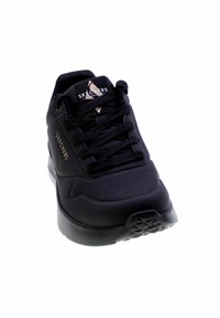 Zwarte sneaker met een glad bovenwerk van synthetisch materiaal, tekstuurelementen, ronde neus, platte veters en een rubberen zool met geometrische looppatronen.