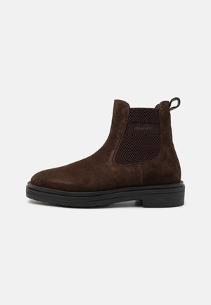Brown suede Chelsea boots with elastic side panels and a pull tab, featuring a textured black rubber sole and a rounded toe.