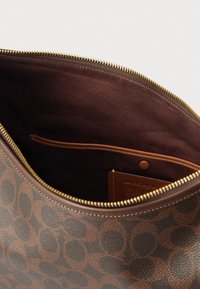 Intérieur d'un sac en cuir marron avec une doublure en tissu marron lisse, une fermeture éclair dorée et une petite poche avec un détail en cuir beige.