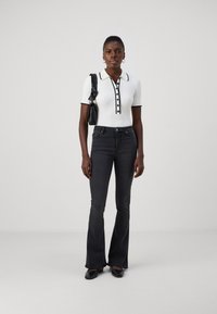 Polo bianco a righe con maniche corte, dettagli e bottoni neri, abbinato a jeans svasati scuri e ballerine nere, completato da una borsa nera.