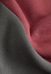 Baumwollstoff in zwei Farben: glattes Grau und sanftes Rosé. Die Textur ist gestrickt mit einer feinen Webart, die subtile Farbvariationen zeigt.
