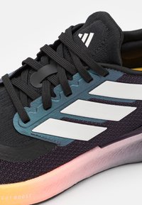 Chaussure de sport noire avec des accents gris, présentant des rayures blanches et une tige texturée. Semelle dégradée de rose à violet avec la marque "LIGHT BOOST".