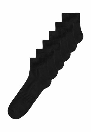 Sechs Paar schwarze Knöchelsocken mit gerippten Bündchen, diagonal auf weißem Hintergrund gestapelt.