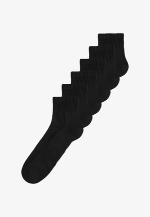 Sechs Paar schwarze Knöchelsocken mit gerippten Bündchen, diagonal auf weißem Hintergrund gestapelt.