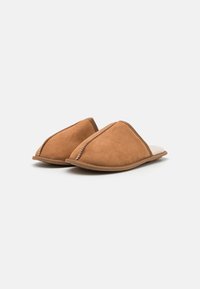 Brown suede slip-on slippers with a soft beige lining, triangular design, and contrasting stitching along the edges.